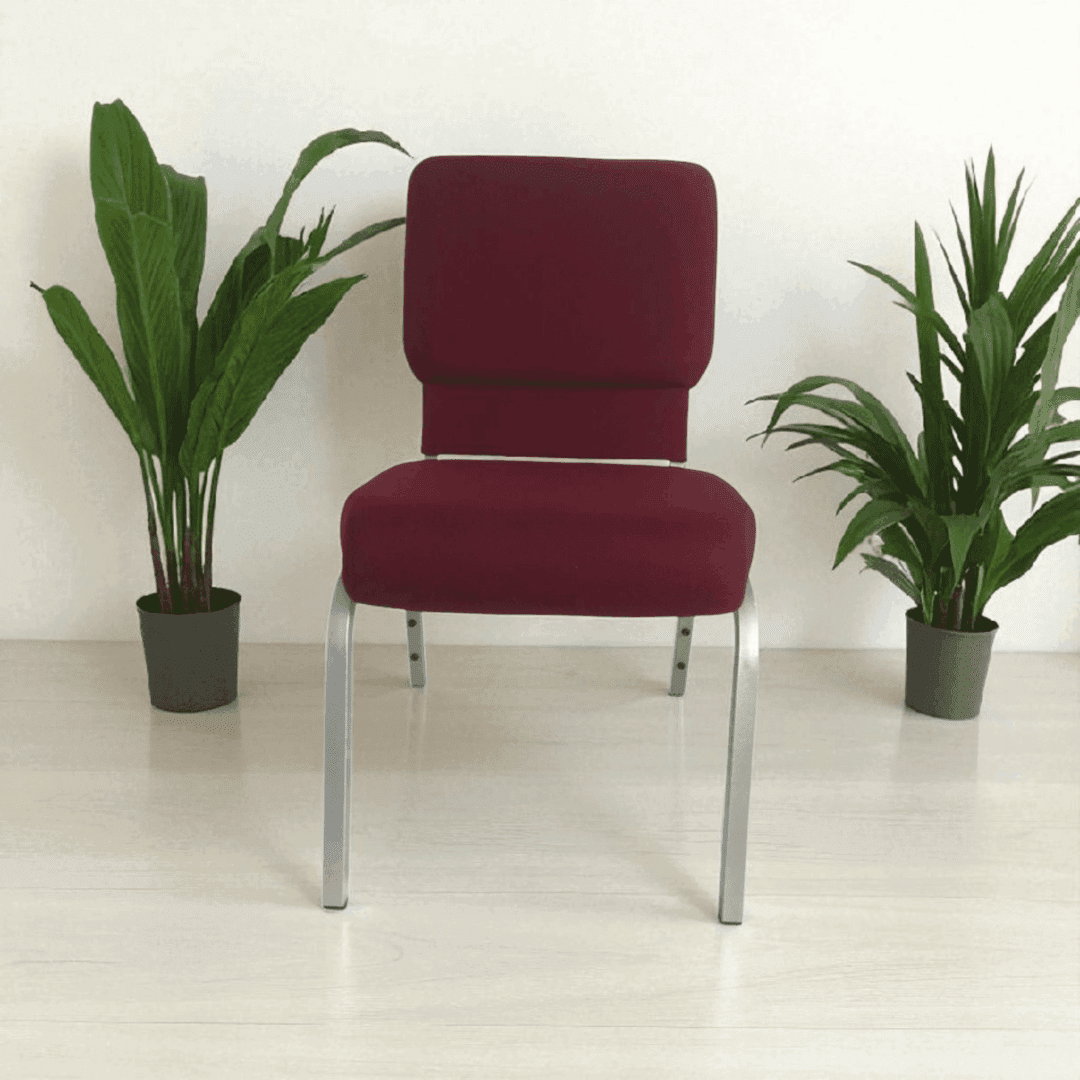 A red cushioned chair with metal legs between two green potted plants.